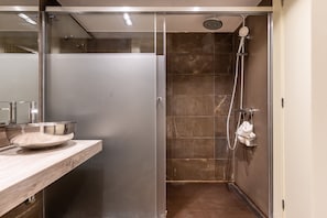 Een moderne badkamer met een douchecabine van glas, een houten wastafelmeubel en een roestvrijstalen wastafel.