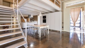 Uma cozinha ampla com eletrodomésticos modernos, uma área de refeições com mesa e cadeiras, e uma escada que dá acesso a um andar superior.