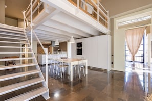 Une cuisine spacieuse équipée d’appareils modernes, un coin repas avec une table et des chaises, et un escalier menant à l’étage supérieur.