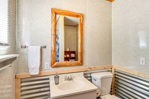 Et badeværelse med et spejl med træramme, en hvid vask og et toilet.