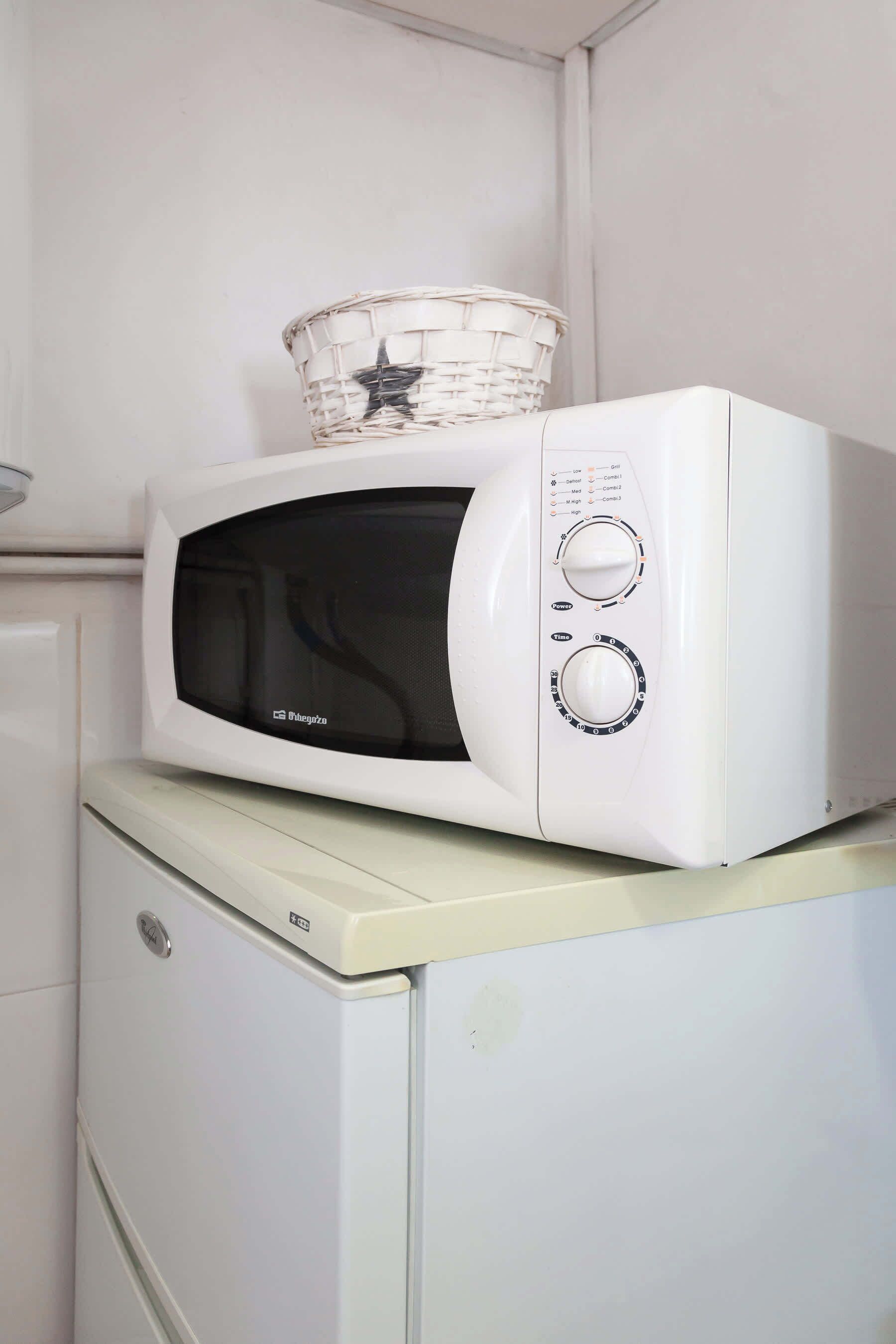 Un four à micro-ondes blanc, surmonté d’un panier, posé sur un appareil électroménager blanc.