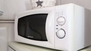 Un four à micro-ondes blanc, surmonté d’un panier, posé sur un appareil électroménager blanc.
