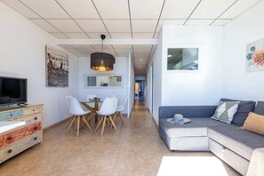 Un salon moderne comprenant un canapé, un téléviseur, un coin repas et des œuvres d’art accrochées aux murs.