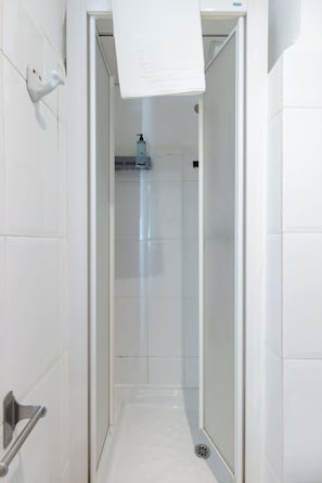 A narrow, tiled bathroom with a shower area, a towel rack, and a hand dryer.