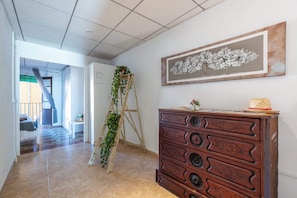 A hallway with a wooden dresser, a ladder with plants, a staircase, and a framed artwork on the wall.