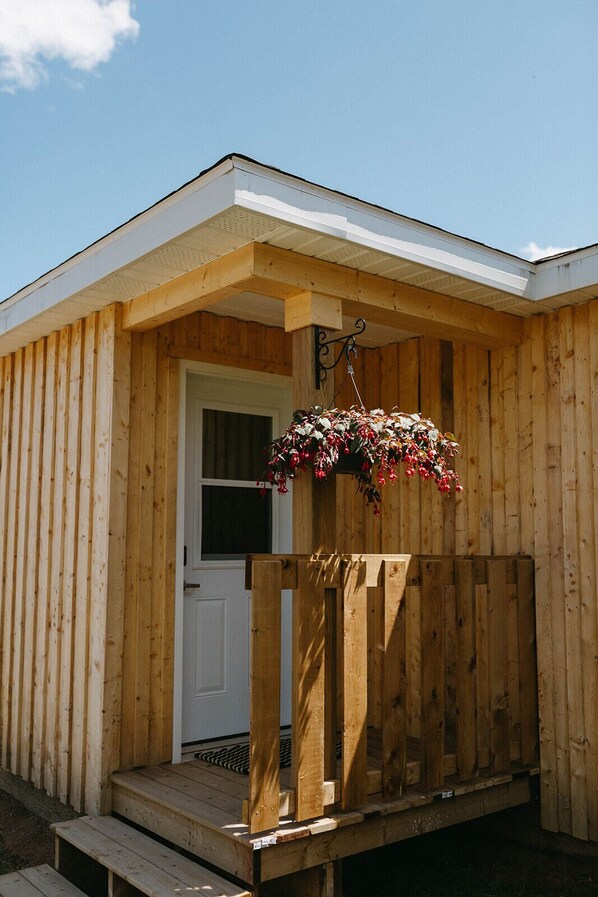 Una cabaña de madera con un porche y una cesta de flores colgante.