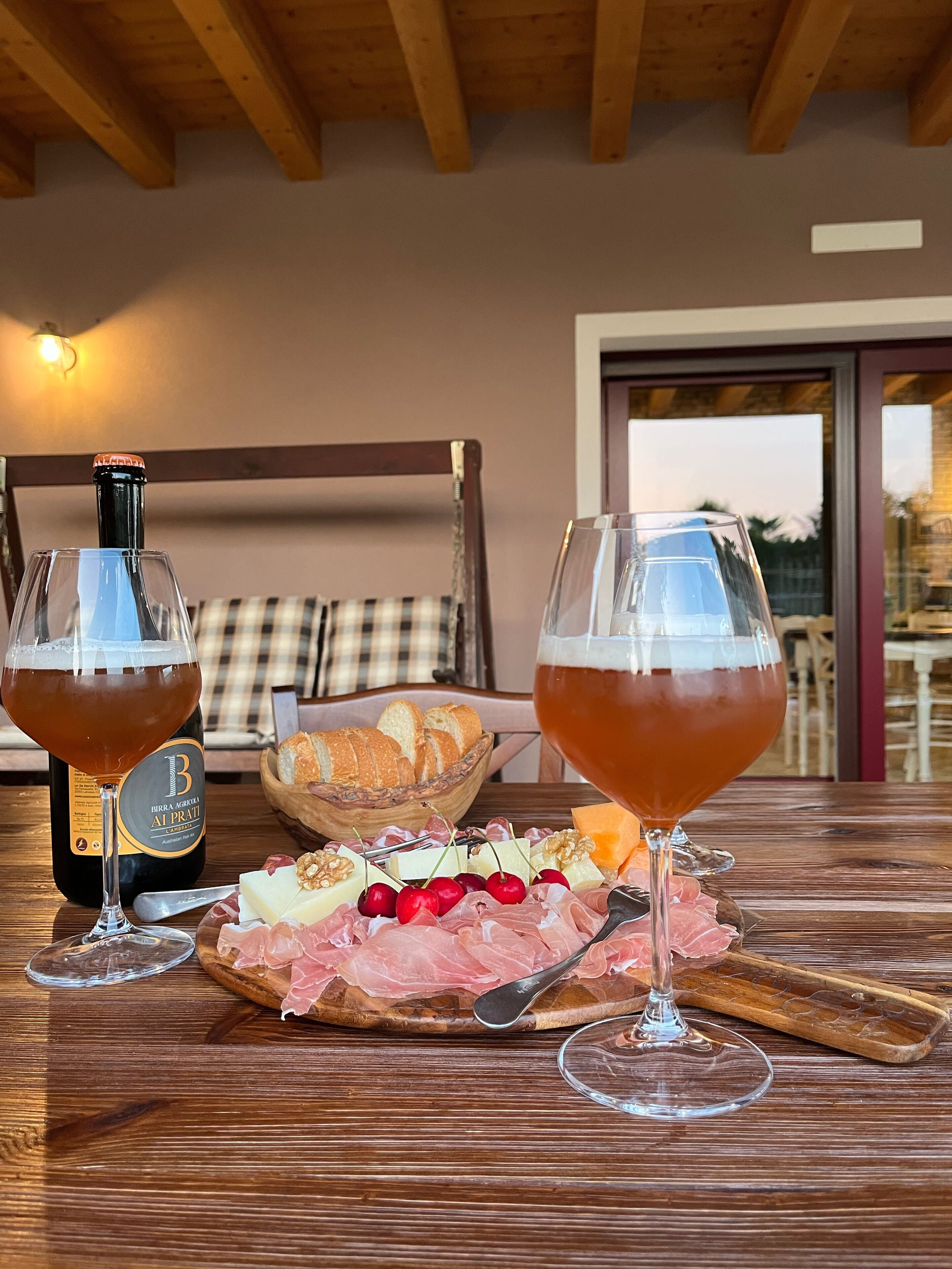 Une table en bois avec deux verres à vin, une bouteille de vin, un panier de pain et une planche de charcuterie garnie de fromage, de noix et de différentes sortes de viande.