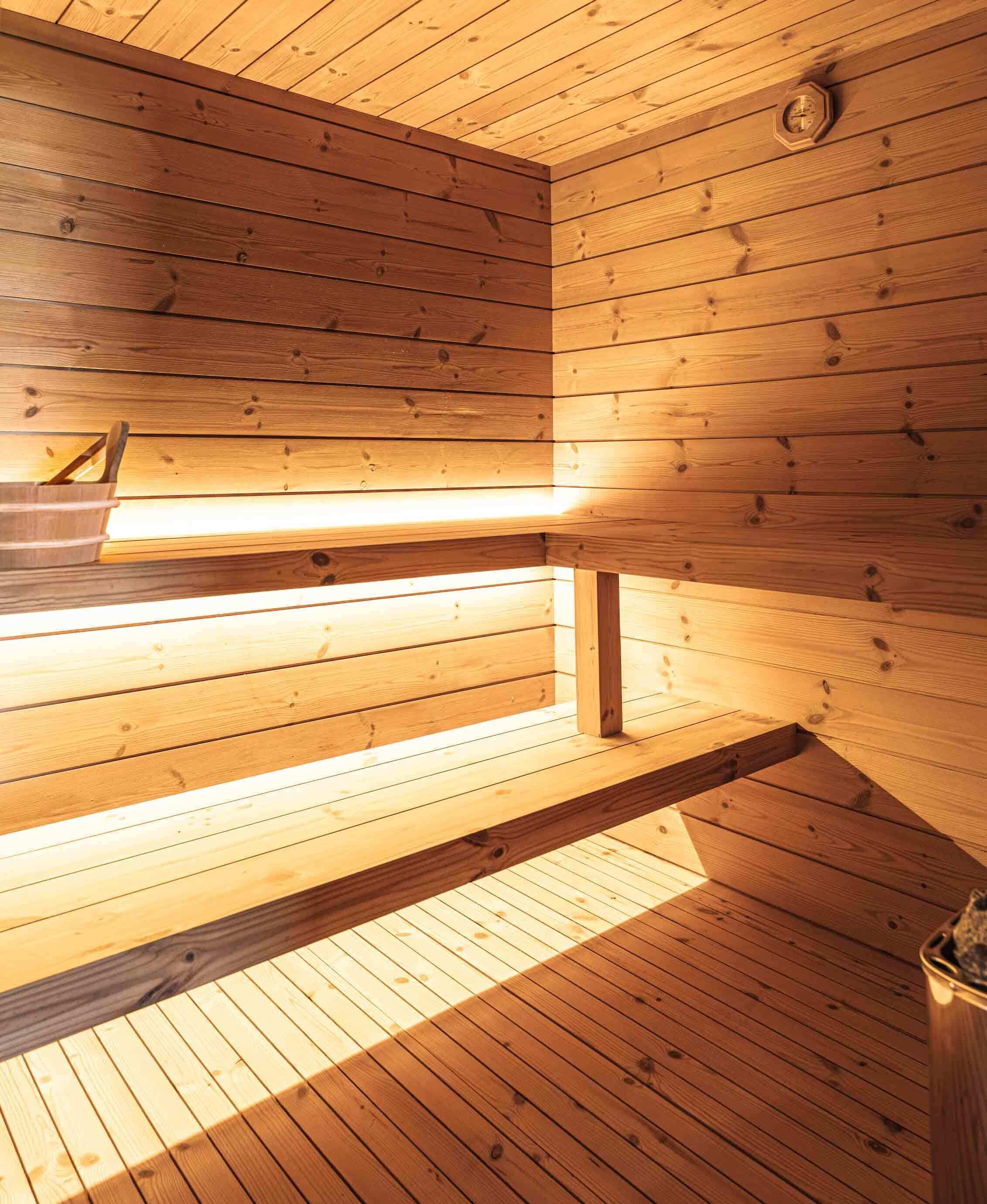 Una sauna con paredes y bancos de madera, techo a la vista y una lámpara.