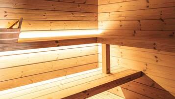 Una sauna con paredes y bancos de madera, techo a la vista y una lámpara.