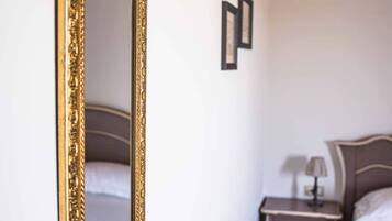 Un dormitorio con un espejo grande y ornamentado, una cama con colcha estampada, una mesita de noche con lámpara y un cabecero de madera.