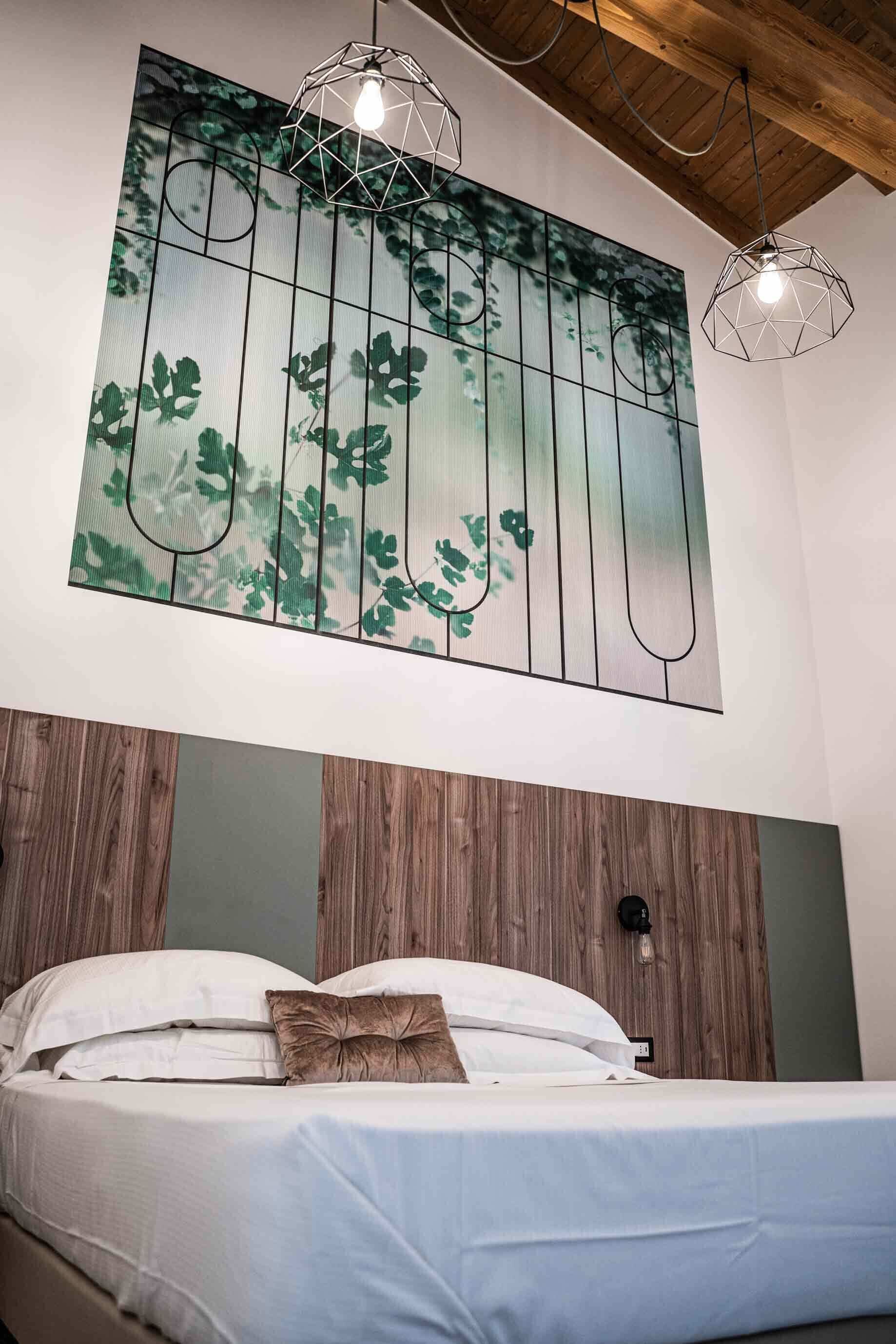 A bedroom with a bed, a wall-mounted artwork of leaves, and two pendant lights.