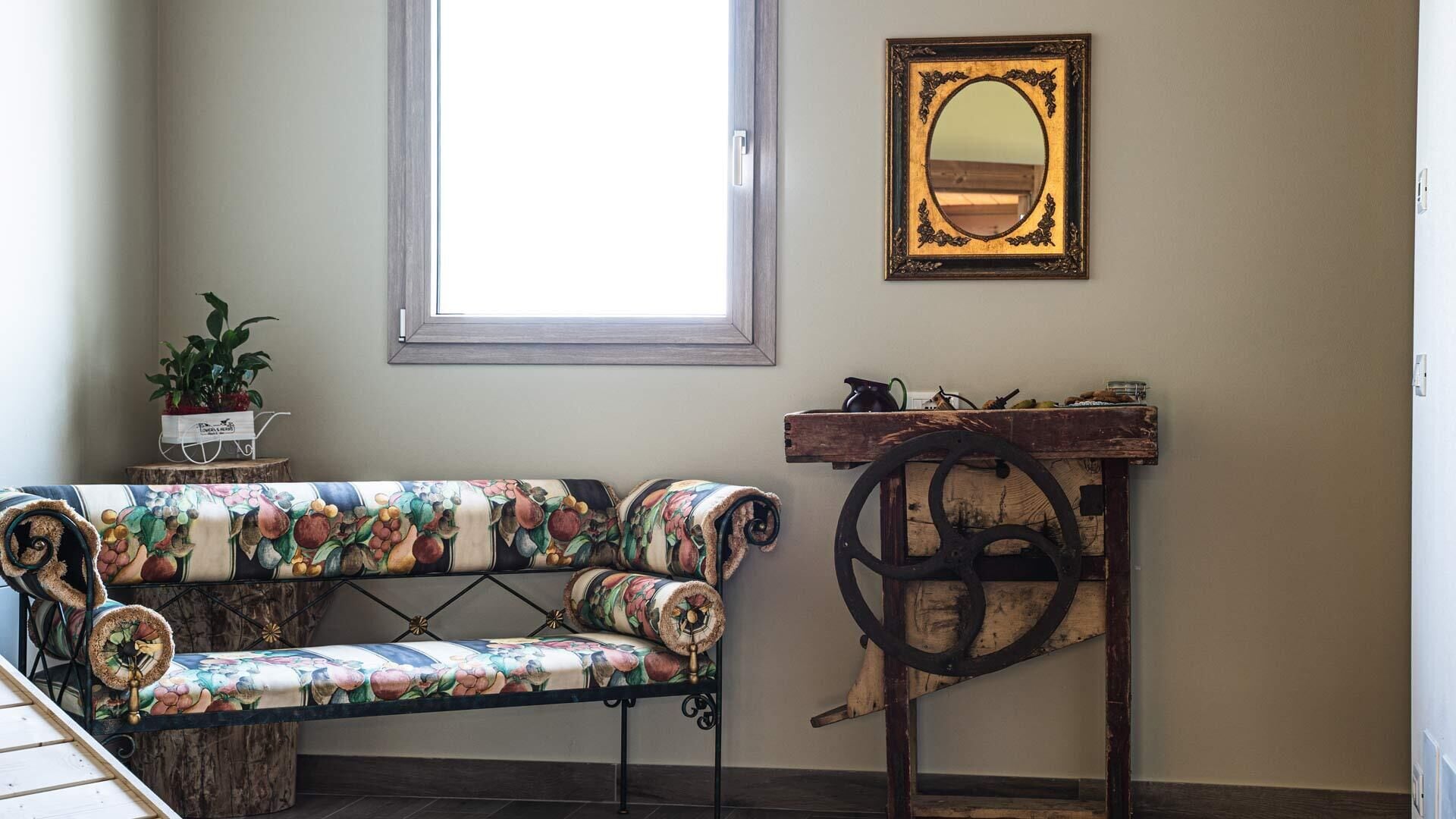 Een knus interieur met een bank met bloemenprint, een houten bijzettafeltje met een antieke wielen, en een spiegel aan de muur.