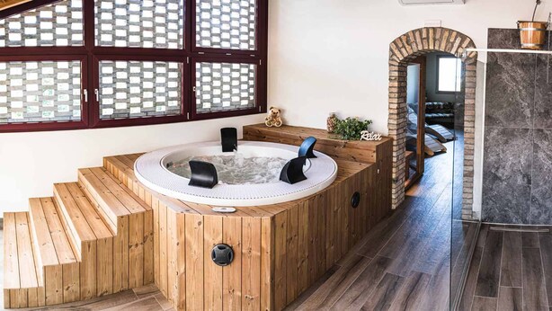 A wooden hot tub with steps leading up to it, a brick archway, and a view of a room with a tiled floor. - Agriturismo Casale ai Prati (Latisana)