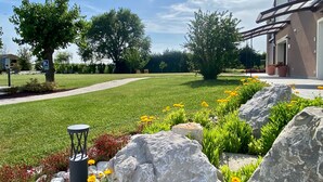 A well-maintained lawn with a pathway, large rocks, and vibrant flowers. - Agriturismo Casale ai Prati (Latisana)