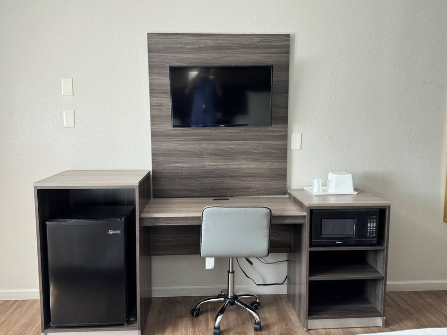 A modern office space with a built-in TV, a refrigerator, a microwave, and a chair.