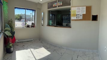 A hotel reception area with a marble floor, a window with a view of the street, and various posted notices.