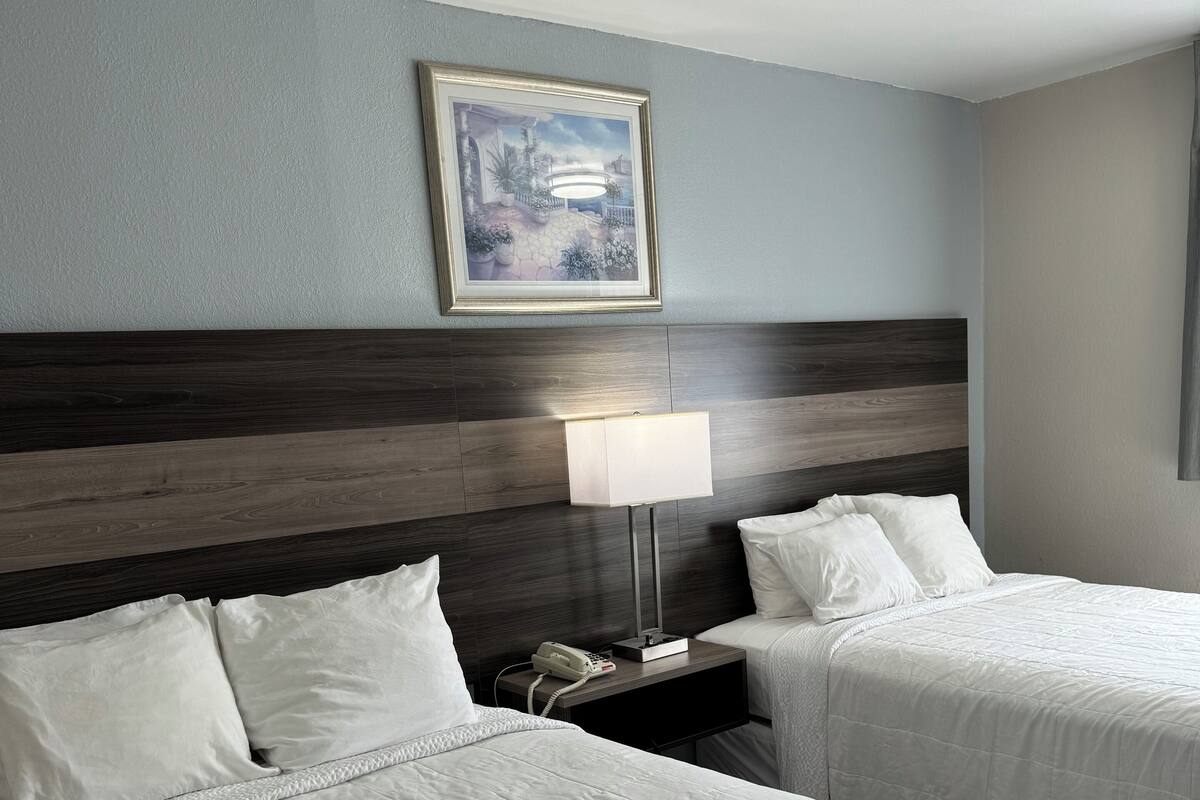 A hotel room with two beds, a nightstand with a lamp, and a framed picture on the wall.