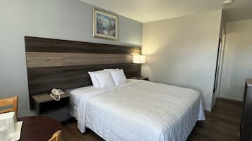 A hotel room with a large bed, a wooden headboard, a bedside table with a lamp, a phone, and a painting on the wall.