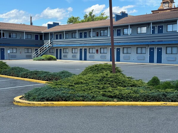 A motel with a parking lot, a staircase leading to the entrance, and a row of rooms with doors.