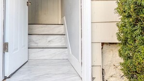 A narrow, white-walled hallway leading to a door with a small, white staircase. - Modern 2 Bedroom in Black Rock (Bridgeport)