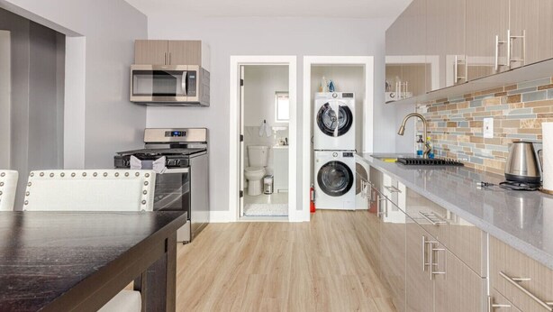A modern kitchen with a microwave, oven, and washing machine, wooden cabinets, and a tiled backsplash. - Modern 2 Bedroom in Black Rock (Bridgeport)