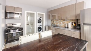 A modern kitchen with stainless steel appliances, a wooden dining table, and a laundry area. - Modern 2 Bedroom in Black Rock (Bridgeport)