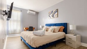 A modern hotel room with a large bed, a desk, a chair, a TV, and an air conditioning unit. - Modern 2 Bedroom in Black Rock (Bridgeport)