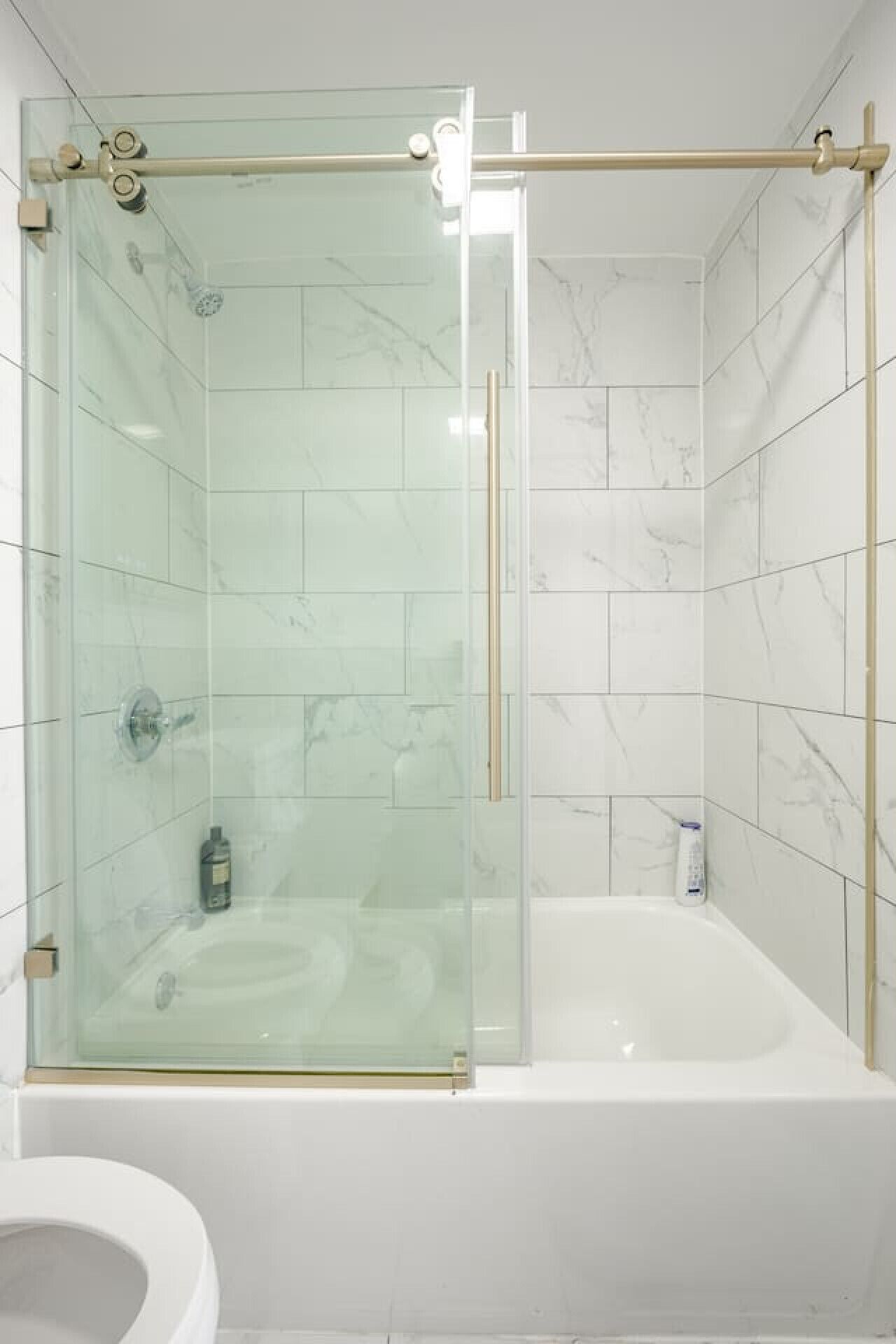 A modern bathroom with a glass-enclosed shower, a white bathtub, and a toilet.