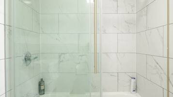 A modern bathroom with a glass-enclosed shower, a white bathtub, and a toilet.