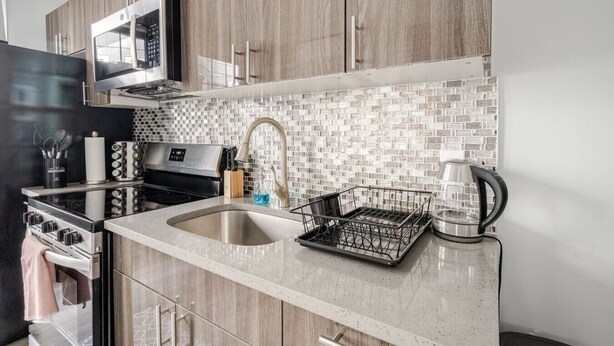 A modern kitchen with wooden cabinets, a stainless steel sink, a microwave, a kettle, and a dish rack. - Modern 2 Bed in BlackRock (Bridgeport)