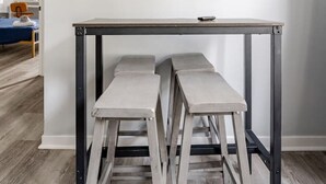 A room with a white air conditioner, a framed artwork of a beach scene, and a wooden table with two stools. - Modern 2 Bed in BlackRock (Bridgeport)