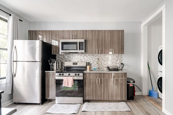 Une cuisine moderne équipée d’un réfrigérateur en acier inoxydable, d’un four à micro-ondes, d’une cuisinière et de meubles de rangement en bois.
