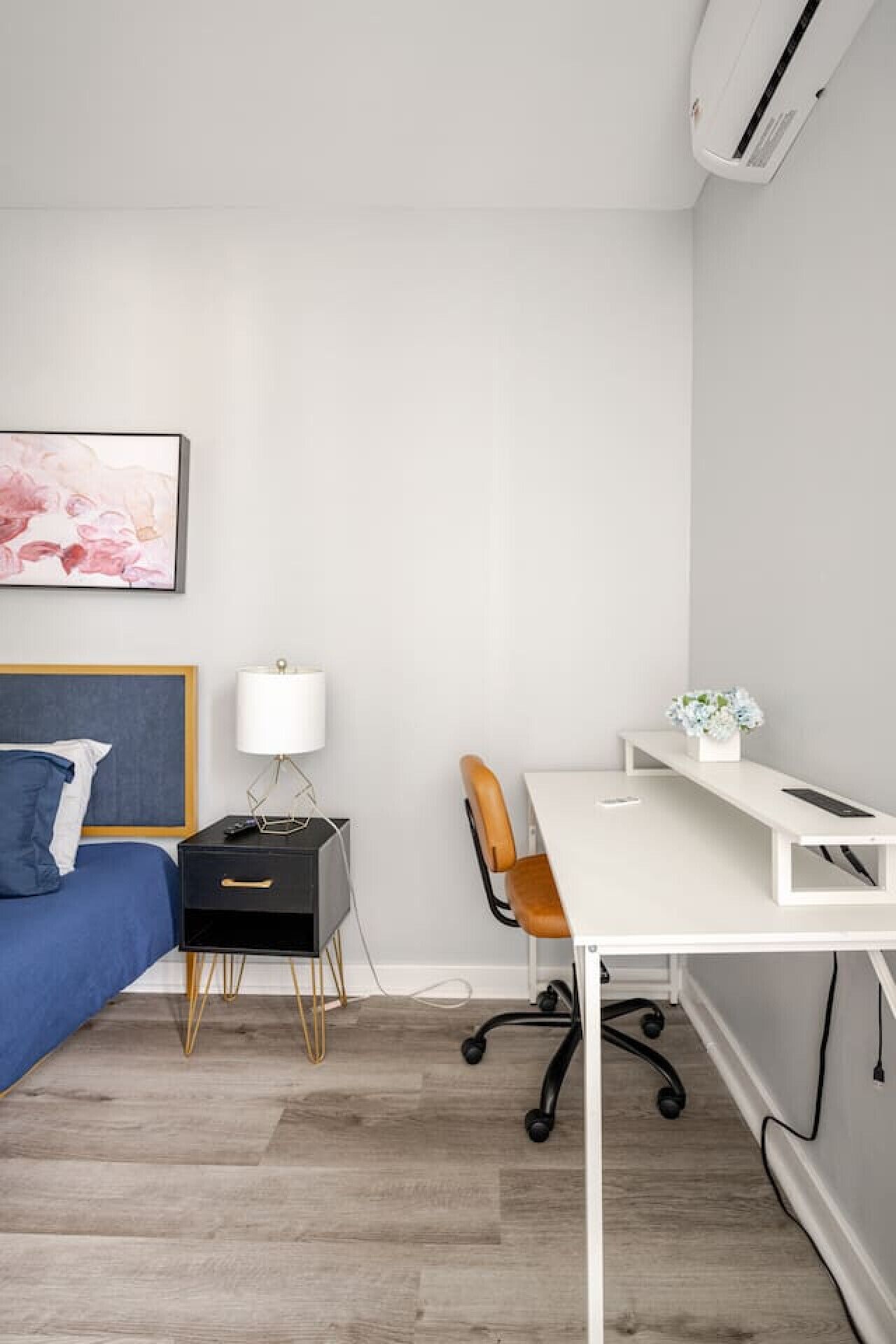 Une chambre à coucher comprenant un lit, un bureau, une chaise, une lampe et un climatiseur fixé au mur.