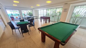 A pool table with chairs and a table in a room with large windows and a view of palm trees. - JARDINS DO ATLANTICO by Penareia.tur.br (João Pessoa)