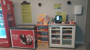 Un quiosco de autoservicio con un refrigerador Coca-Cola, un congelador Plusvita y una vitrina refrigerada con aperitivos.