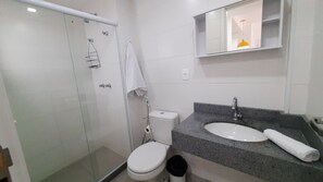 Un baño con cabina de ducha de vidrio, inodoro blanco, lavamanos con encimera de granito y espejo sobre el lavamanos.