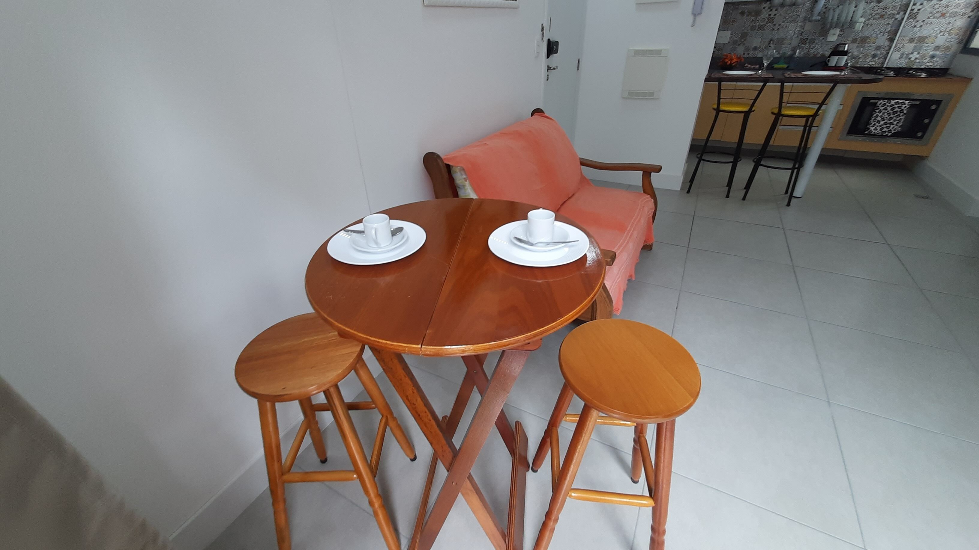 A dining area with a round wooden table set for two, two wooden stools, and a pink sofa in the background.