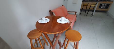 A dining area with a round wooden table set for two, two wooden stools, and a pink sofa in the background.