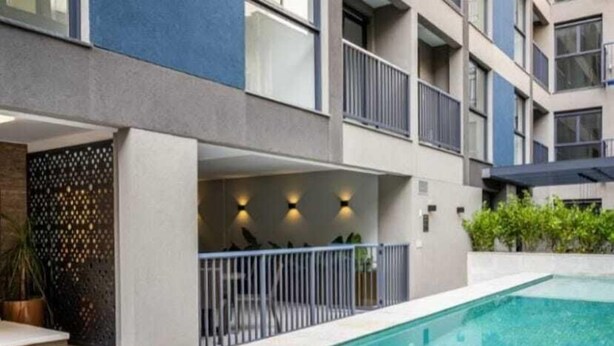 Un edificio moderno con piscina, sillas de descanso y un balcón con barandillas.