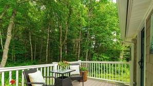 Eine Holzterrasse mit Korbmöbeln und einem weißen Geländer, mit Blick auf eine bewaldete Landschaft.