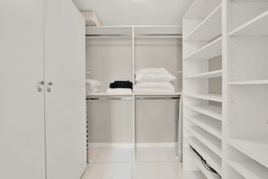 A white closet with shelves and hanging space, a white door, and a tiled floor.