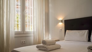 Une chambre d’hôtel avec un lit, une table de chevet, une lampe fixée au mur et une fenêtre avec des rideaux.