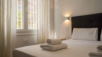 Una habitación de hotel con una cama, una mesita de noche, una lámpara de pared y un ventanal con cortinas.