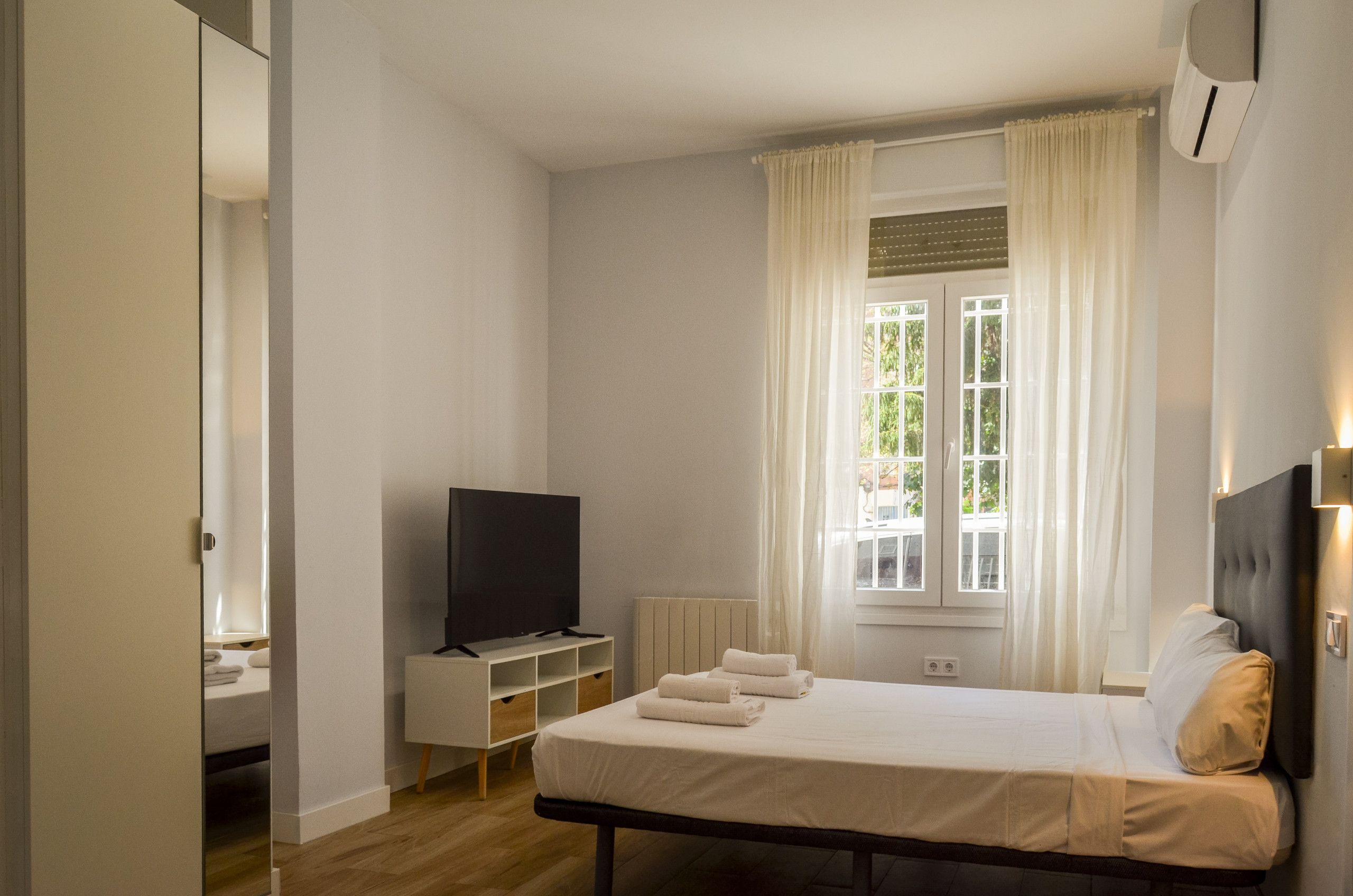 Una habitación de hotel con una cama, televisión, ventana con cortinas y un radiador.