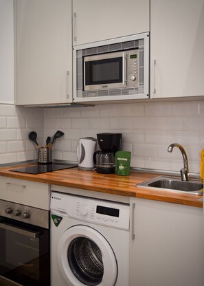 Een keuken met een magnetron, koffiezetapparaat en een wasmachine.