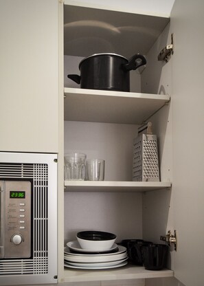 Een keuken met een magnetron, planken met servies en een pan.