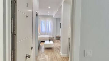 Een gang die leidt naar een slaapkamer met een bed, een nachtkastje en een kleine bedlamp.