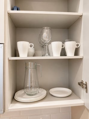 Un meuble de cuisine avec des étagères blanches contenant des tasses blanches, un pichet en verre et des assiettes.