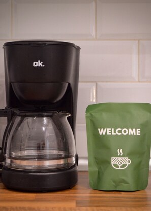 A black coffee maker and a green welcome bag on a kitchen counter.