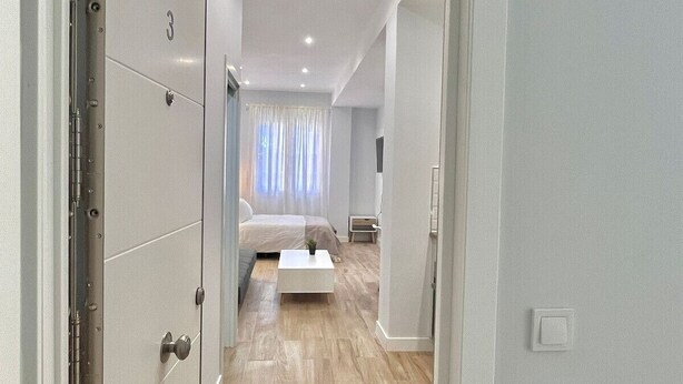 Un pasillo que conduce a un dormitorio con cama, mesita de noche y una lámpara de noche pequeña.